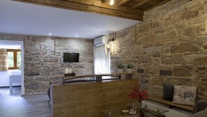 Un intérieur rustique avec des murs en pierre, un banc en bois et une table en verre ornée d’un vase de fleurs.