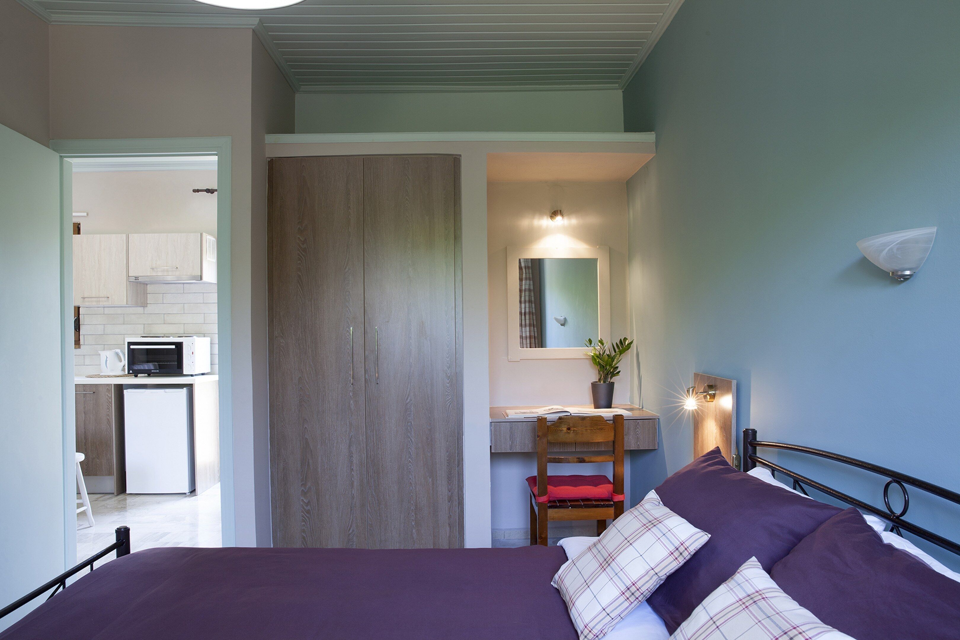 A bedroom with a bed, a desk, and a kitchenette.