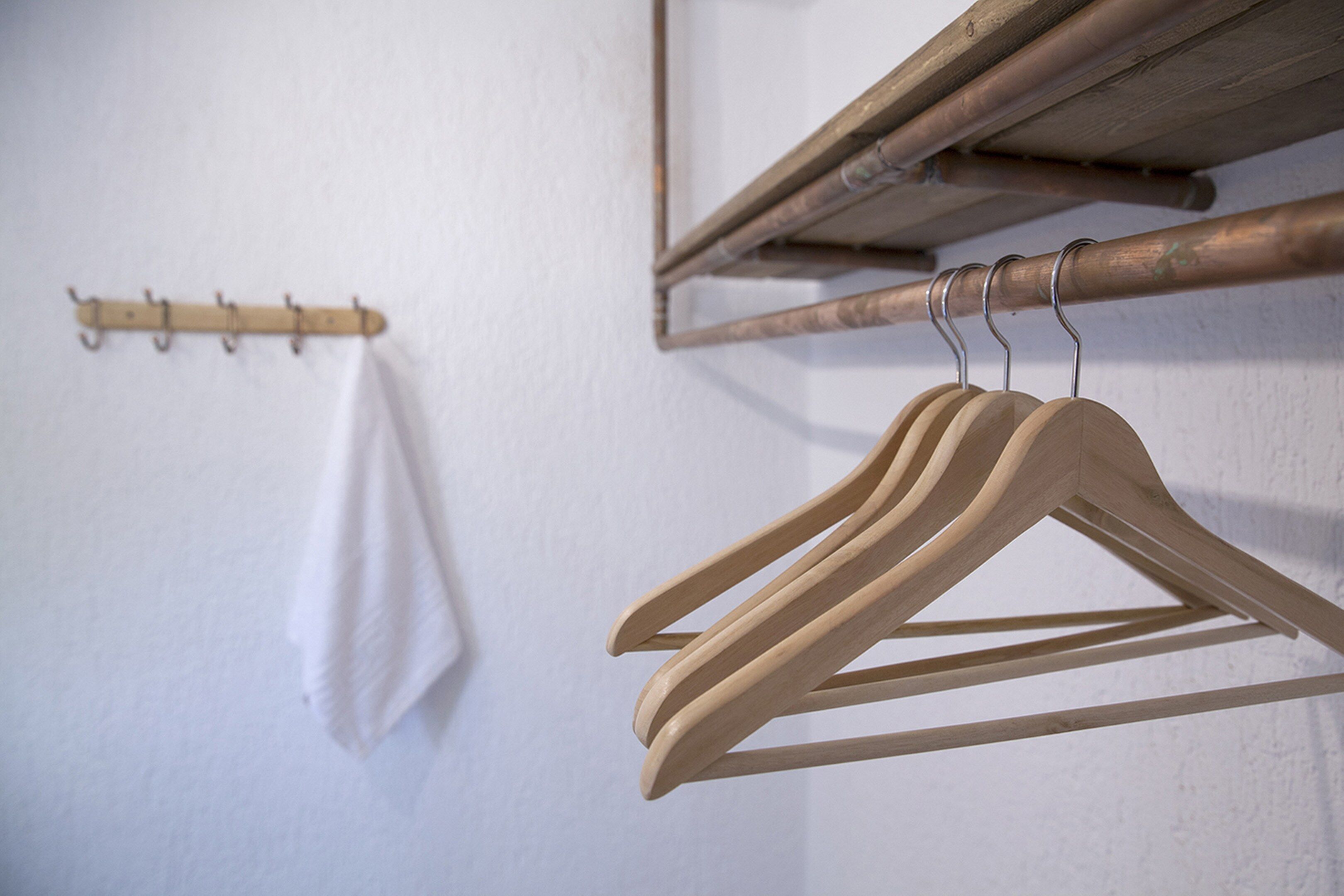 Wooden hangers on a wall-mounted rack, a wooden coat rack, and a white towel hanging on a hook.