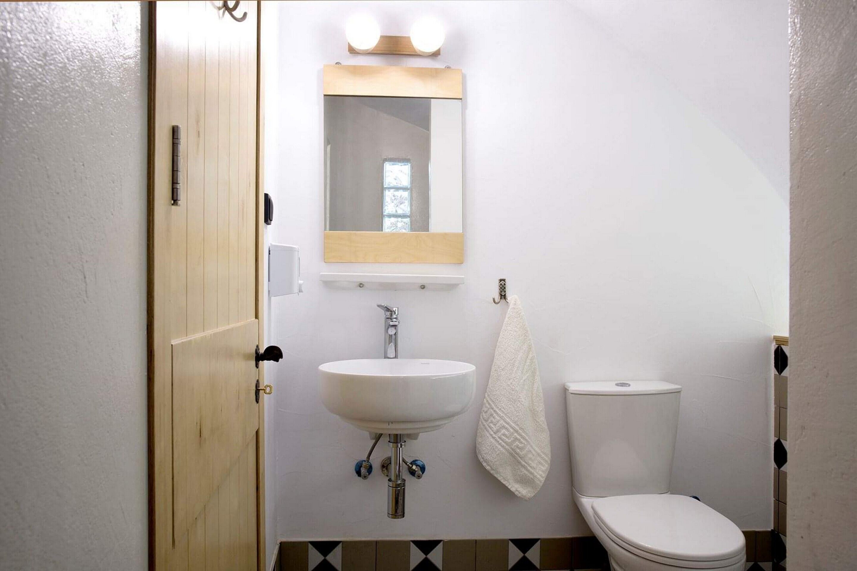A bathroom with a wooden door, a white sink, a mirror, and a toilet.