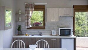 Une cuisine équipée d’un four à micro-ondes, d’un évier et de placards. Une fenêtre offre une vue sur la verdure environnante.
