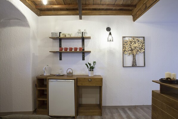 A compact kitchen with a wooden counter, a small refrigerator, and shelves with kitchenware.