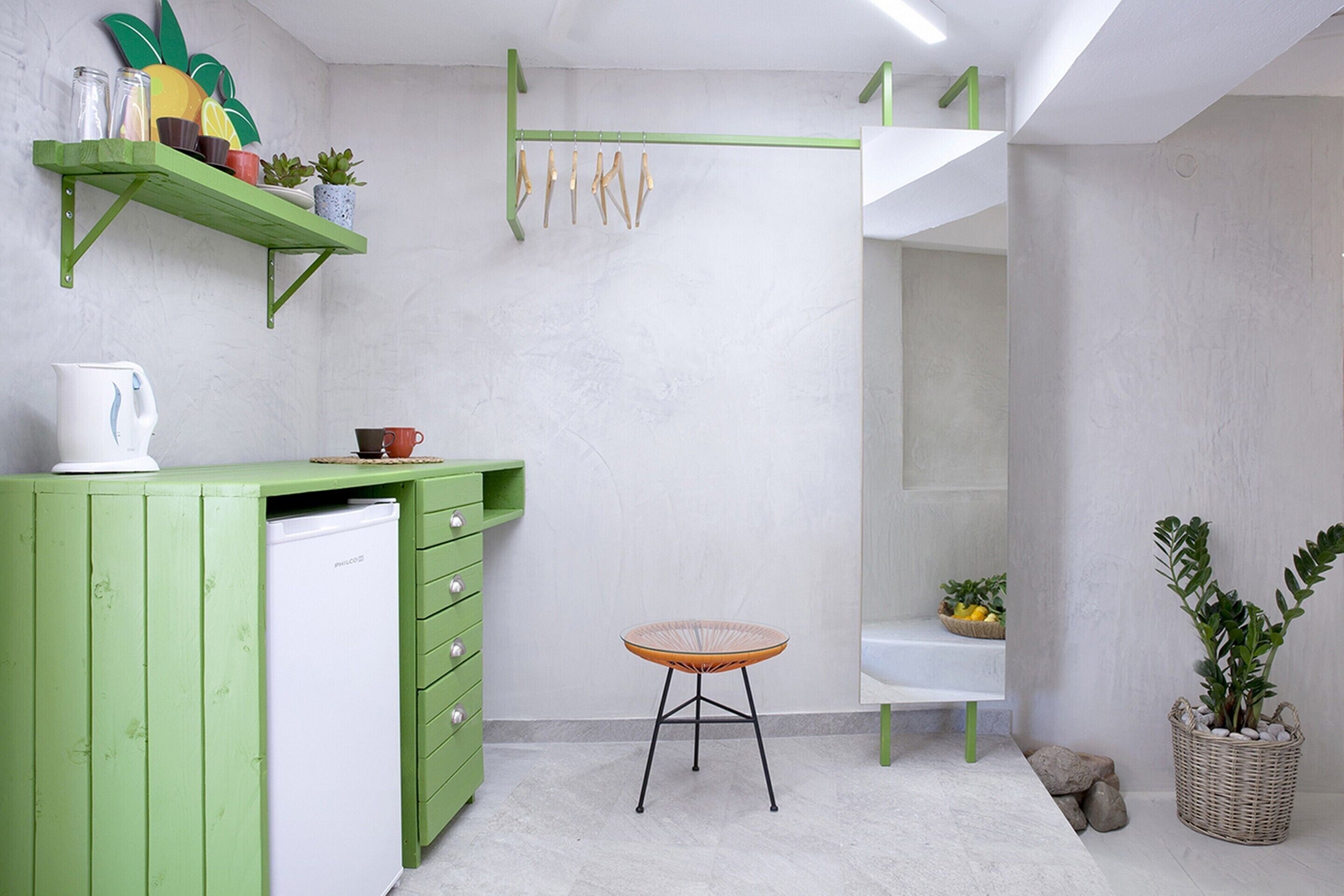 A compact kitchen with a green countertop, a white refrigerator, a wicker chair, and a hanging rack with wooden utensils.