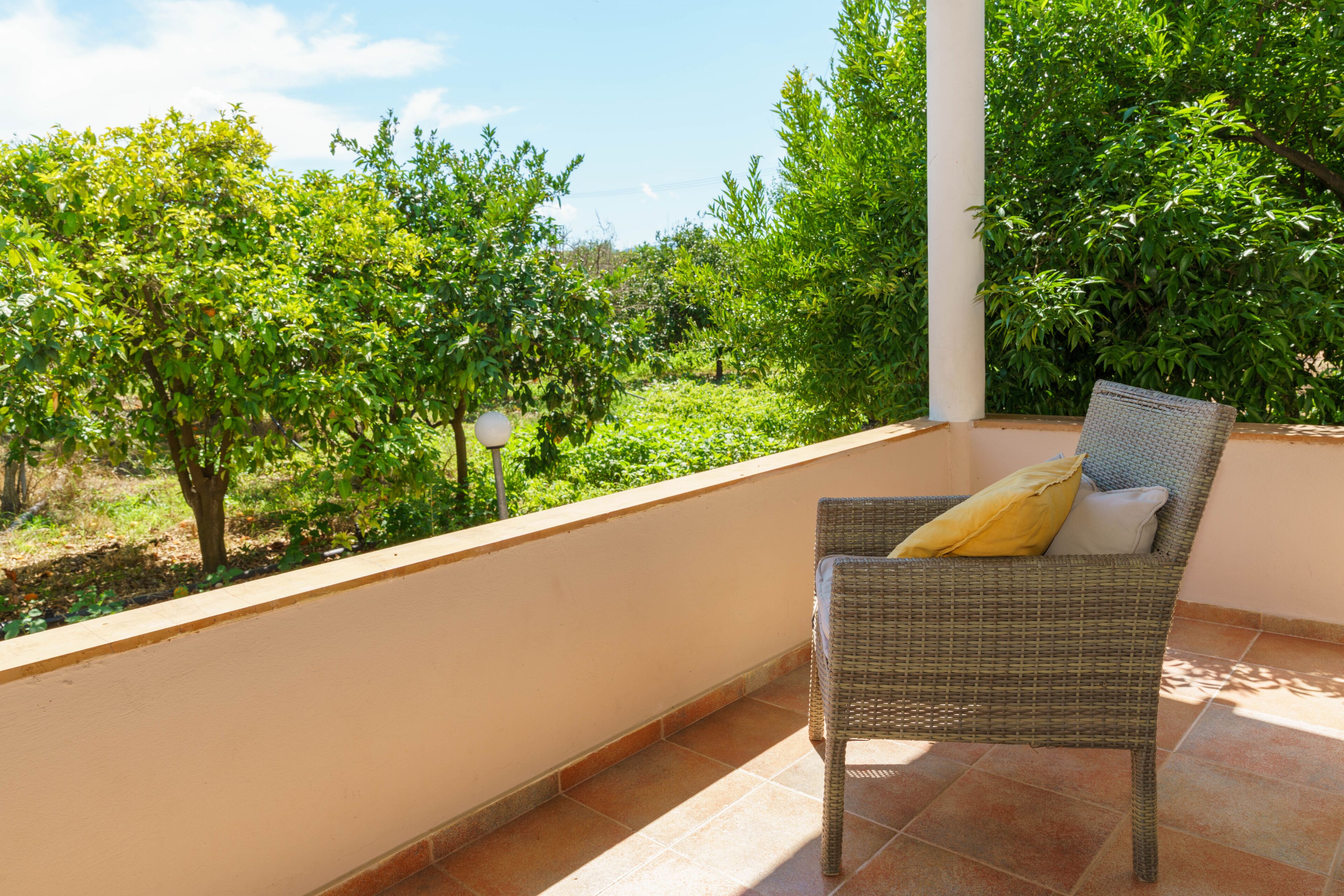 A wicker chair with a cushion on a balcony with a view of a garden and trees.