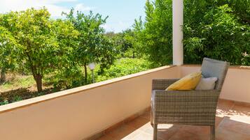 A wicker chair with a cushion on a balcony with a view of a garden and trees.