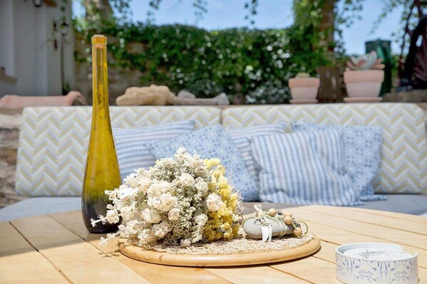 A table with a bottle, a floral arrangement, a small decorative item, and a candle holder. - Voulamandis House (Chios)