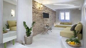 Un salon moderne avec un mur en pierre, un téléviseur à écran plat, un canapé et une table à manger agrémentée d’un panier de fruits.