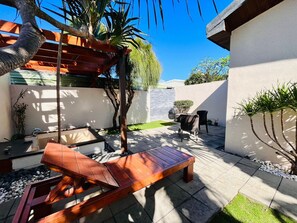 A patio with a wooden bench, a small table, and a hanging chair. There is a wall with a small tree and a potted plant. - Pangola B&B (Hengchun)
