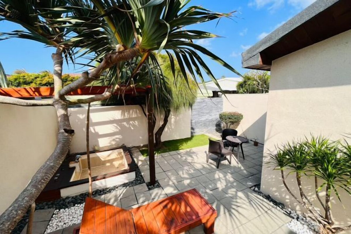 A patio area with a wooden bench, a small table, and a potted plant.