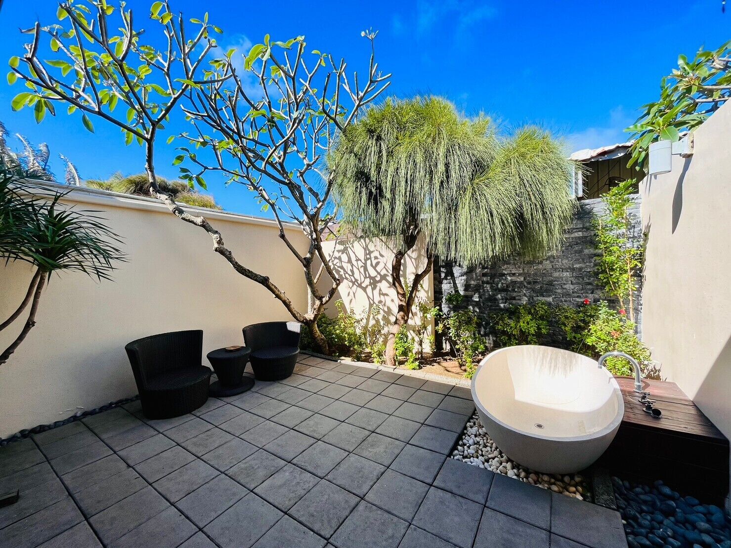 Un patio con un jacuzzi, dos sillas negras y una mesita.