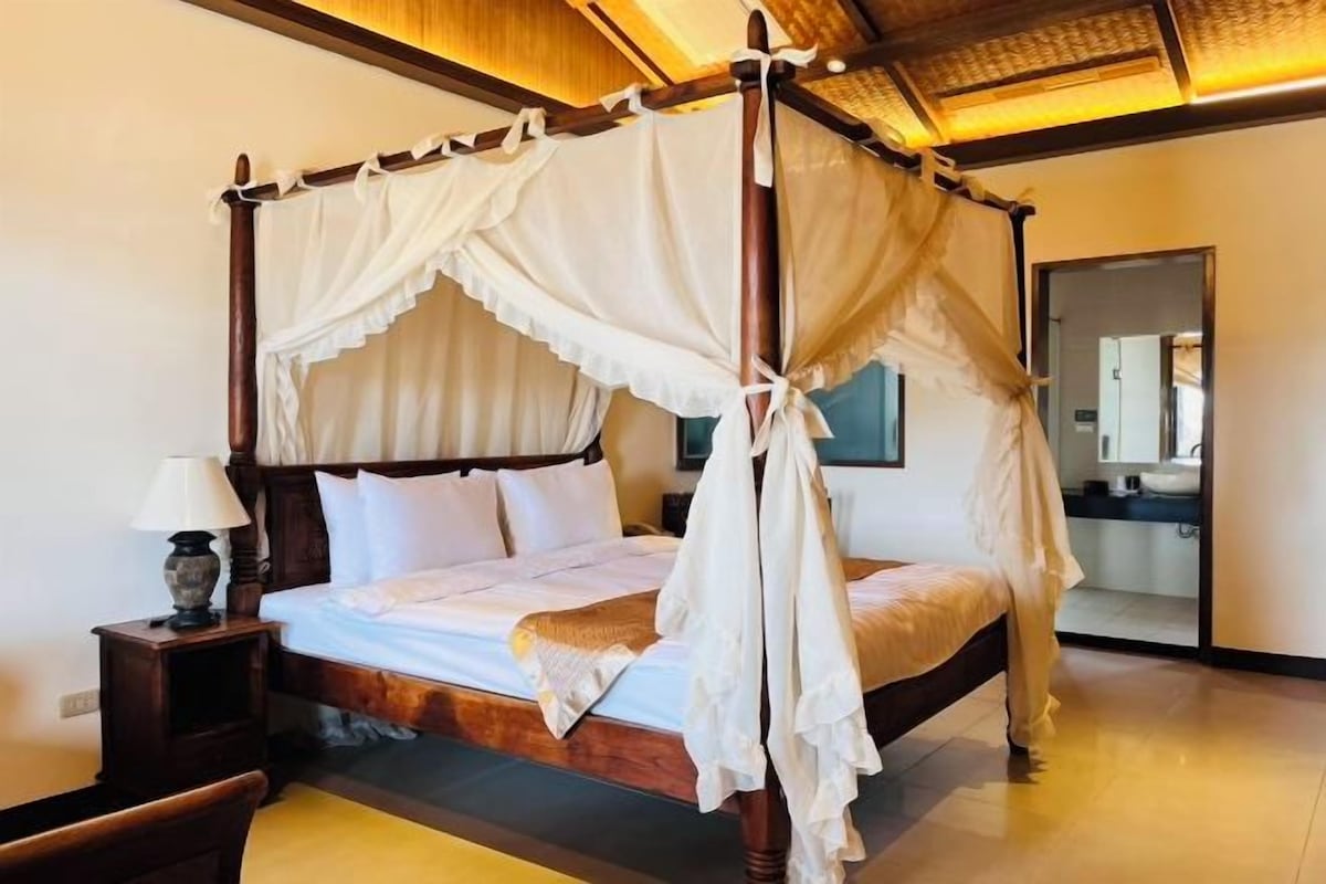 A four-poster bed with a canopy, a bedside table with a lamp, and a mirror on the wall.