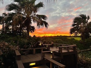A wooden deck with benches overlooking a sunset view, surrounded by palm trees and vegetation. - Pangola B&B (Hengchun)