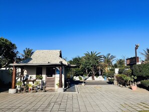 A building with a thatched roof, surrounded by potted plants and palm trees. - Pangola B&B (Hengchun)
