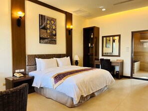 A hotel room with a large bed, a desk, a chair, a telephone, and artwork on the walls. - Pangola B&B (Hengchun)