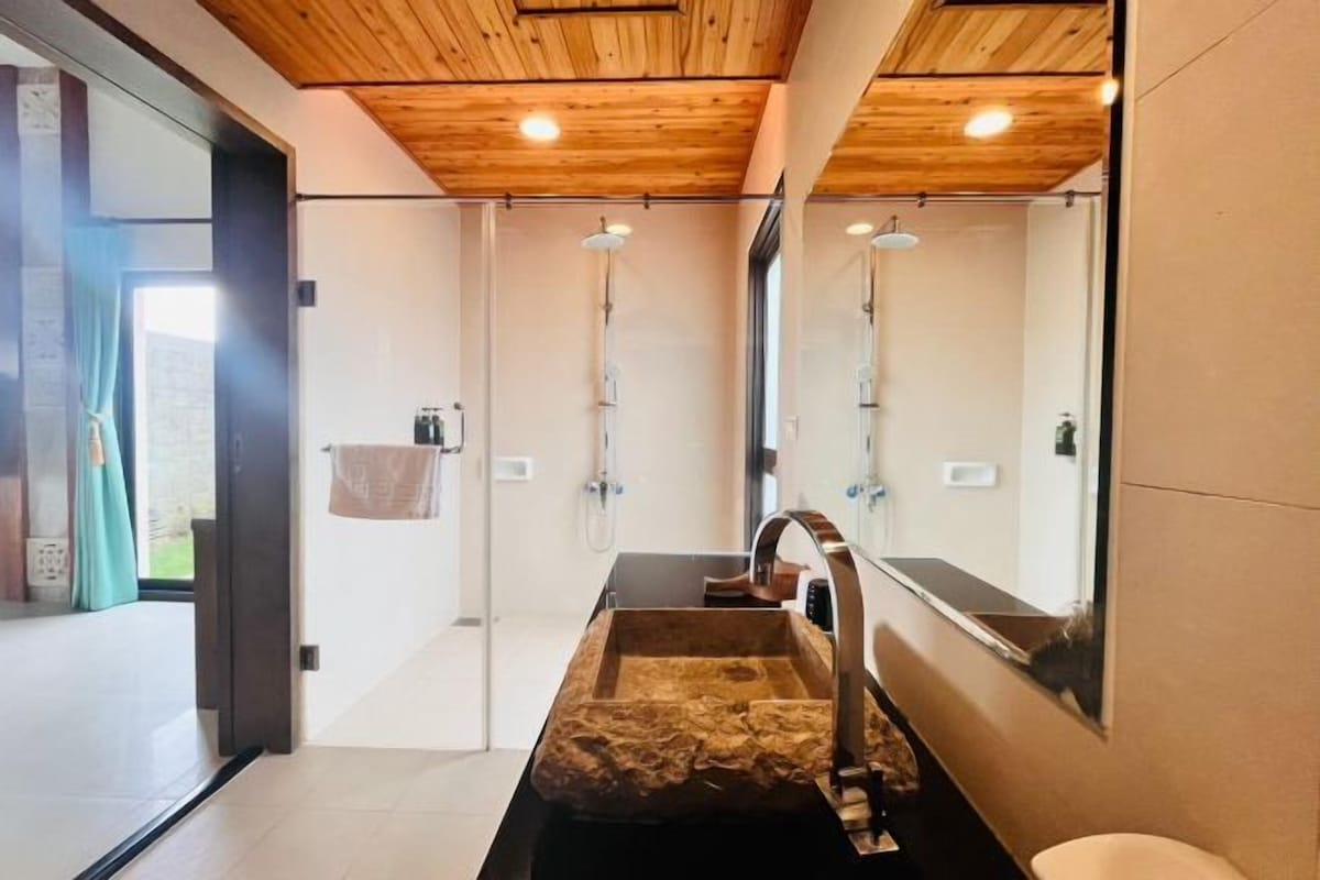 A modern bathroom with a wooden ceiling, a large mirror, a wooden sink, and a shower area.
