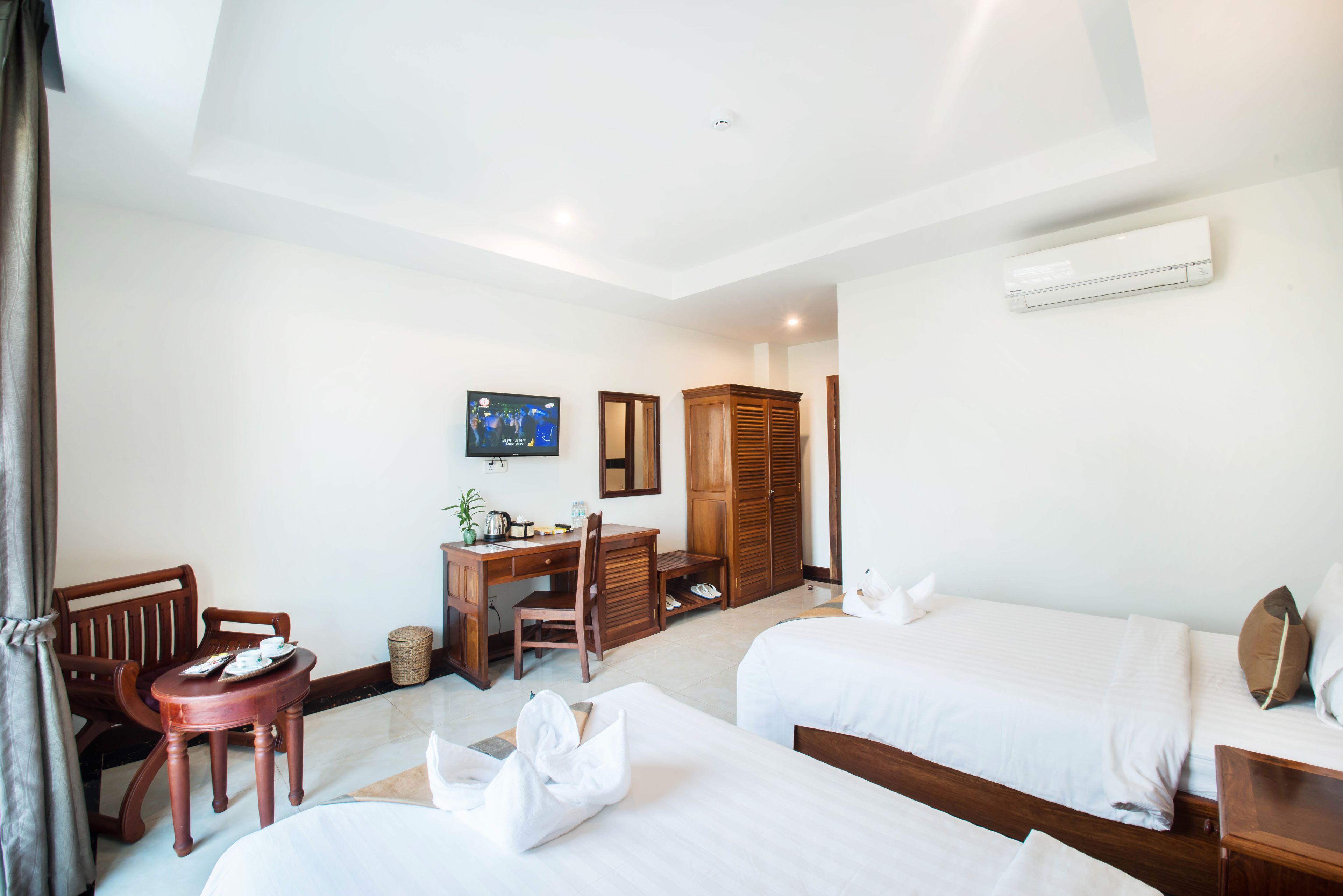 A hotel room with two beds, a desk with a chair, a television, and a wardrobe.