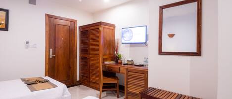 A hotel room with two beds, a wooden wardrobe, a desk with a computer, a chair, and a shoe rack.