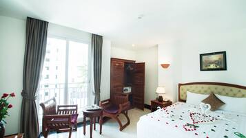 Habitación de hotel con cama, sillón, mesita, mesita de noche, lámpara, un cuadro y vistas al exterior.