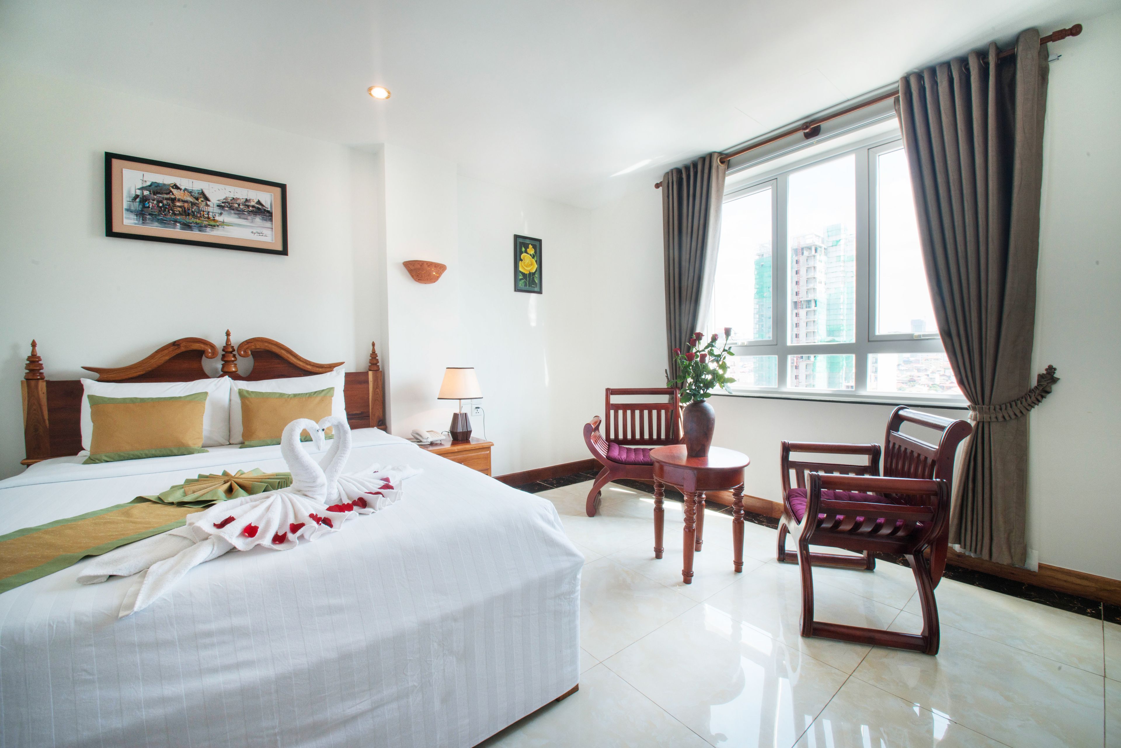 Quarto de hotel com cama bem arrumada, uma cadeira, uma mesa pequena e uma janela com cortinas.