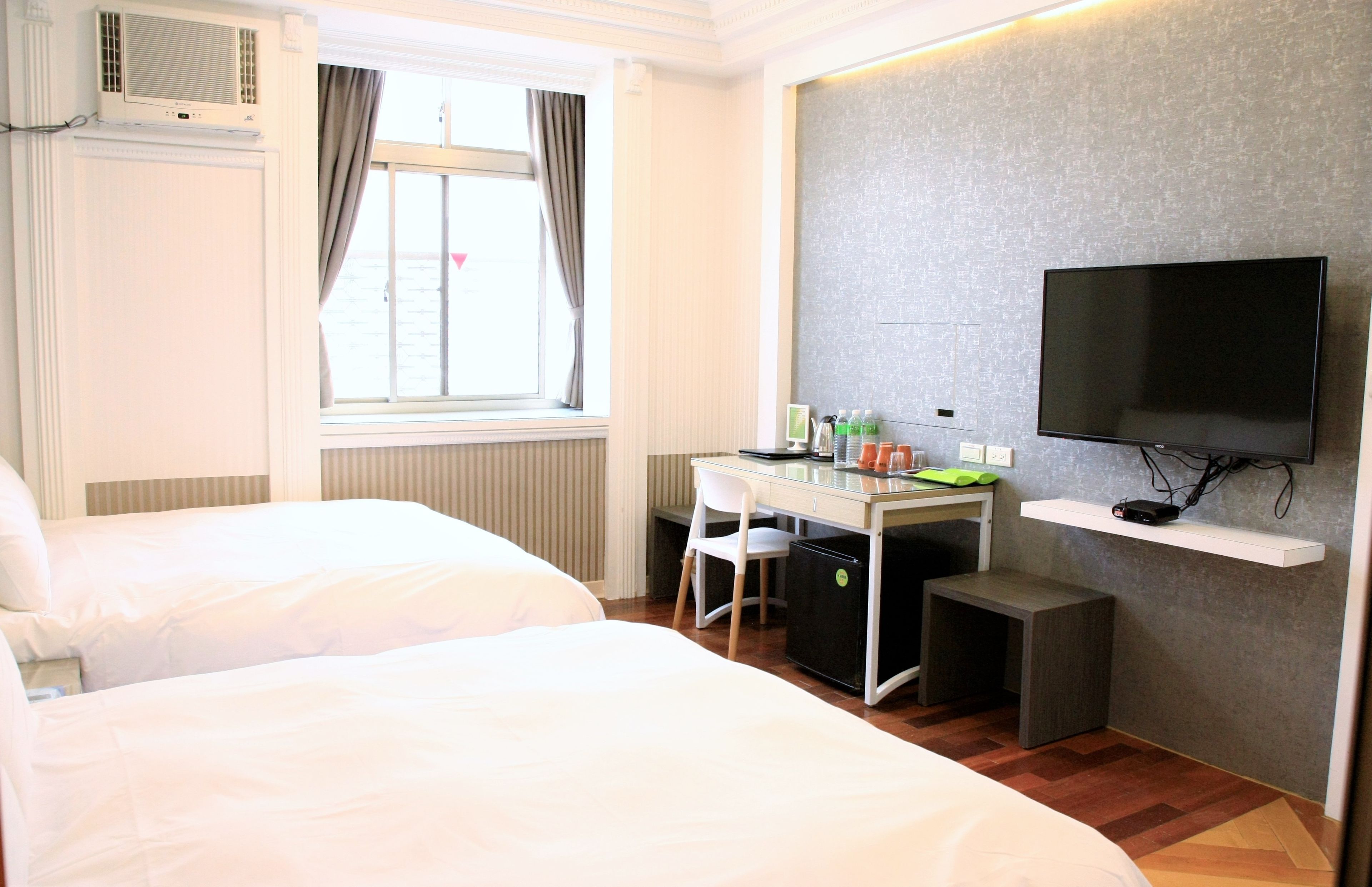 Une chambre d’hôtel avec deux lits, un bureau avec un ordinateur, une télévision et une fenêtre avec des rideaux.