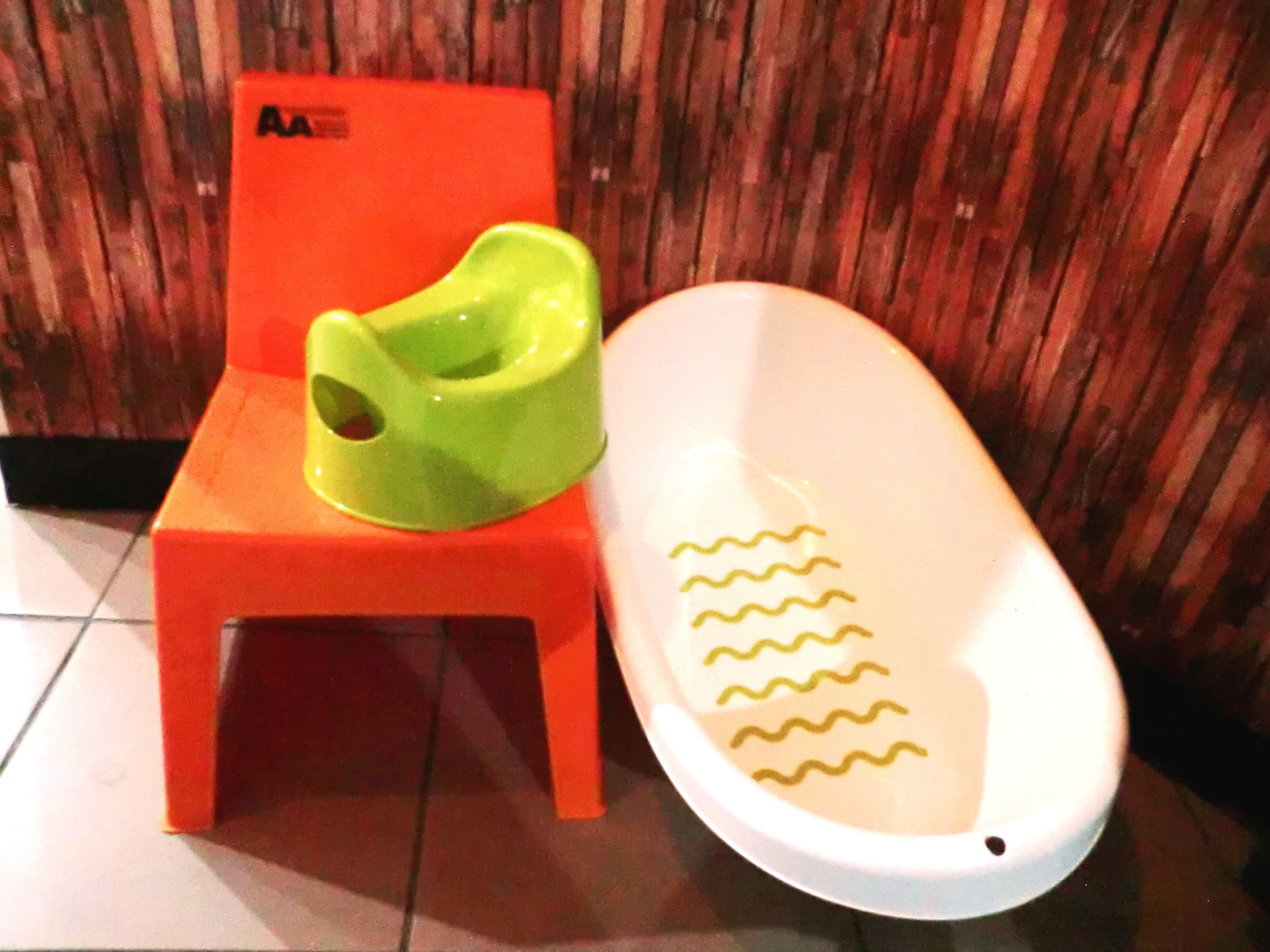 A small orange chair with a green object on it, next to a white bathtub with wavy lines.