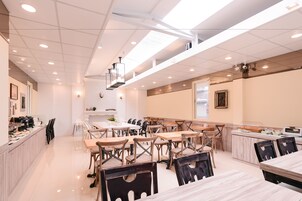 Un comedor amplio con varias mesas y sillas, una pared de ladrillo blanco e iluminación empotrada en el techo.