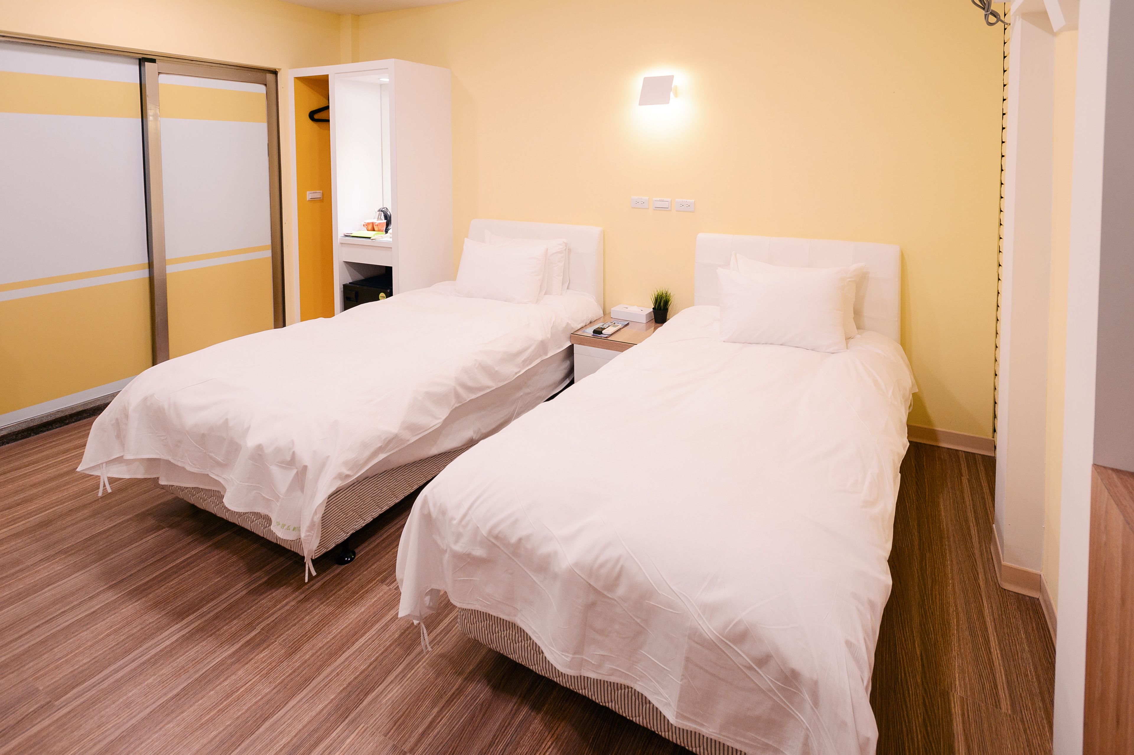 Une chambre d’hôtel avec deux lits simples, un plancher en bois, une porte coulissante et une petite table de chevet avec une lampe.