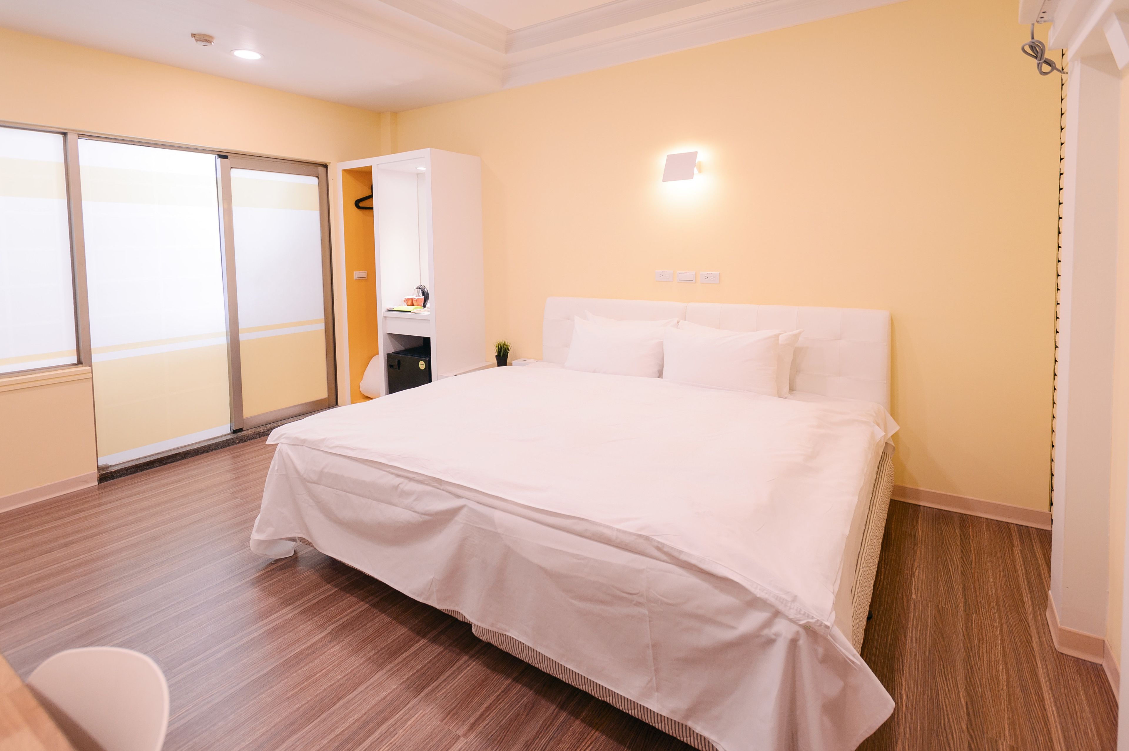 A hotel room with a large bed, a wardrobe, a desk, and a sliding door.