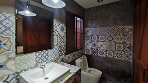 A bathroom with a white sink, a toilet, and a mirror. The walls are decorated with patterned tiles. - Happy Field Resort Cha-am (Cha-am)
