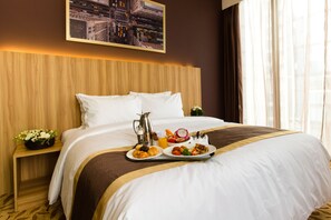Une chambre d’hôtel avec un lit soigneusement fait, un plateau avec des articles pour le petit-déjeuner, un tableau représentant un paysage urbain et une table de chevet ornée d’une fleur.