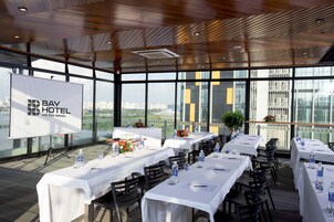 Ein Konferenzraum im Bay Hotel Ho Chi Minh mit gedeckten Tischen für eine Besprechung, großen Fenstern mit Blick auf die Stadt und einem modernen Deckenstil.