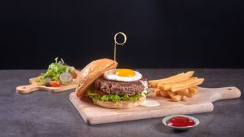 A burger with a fried egg on a wooden board, accompanied by fries and a small bowl of ketchup.