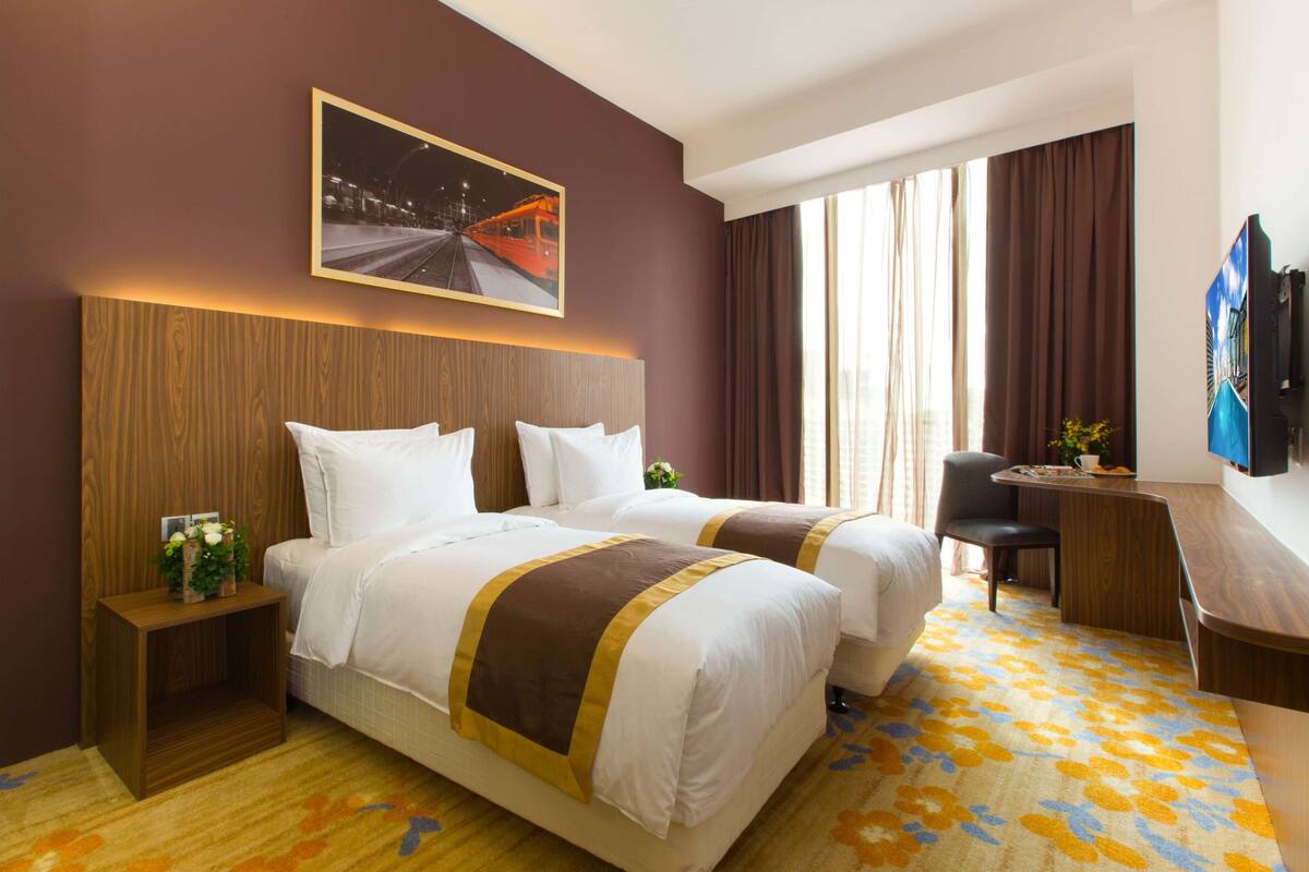 Ein Hotelzimmer mit zwei Betten, einem Schreibtisch, einem Sessel und einem an der Wand befestigten Fernseher.