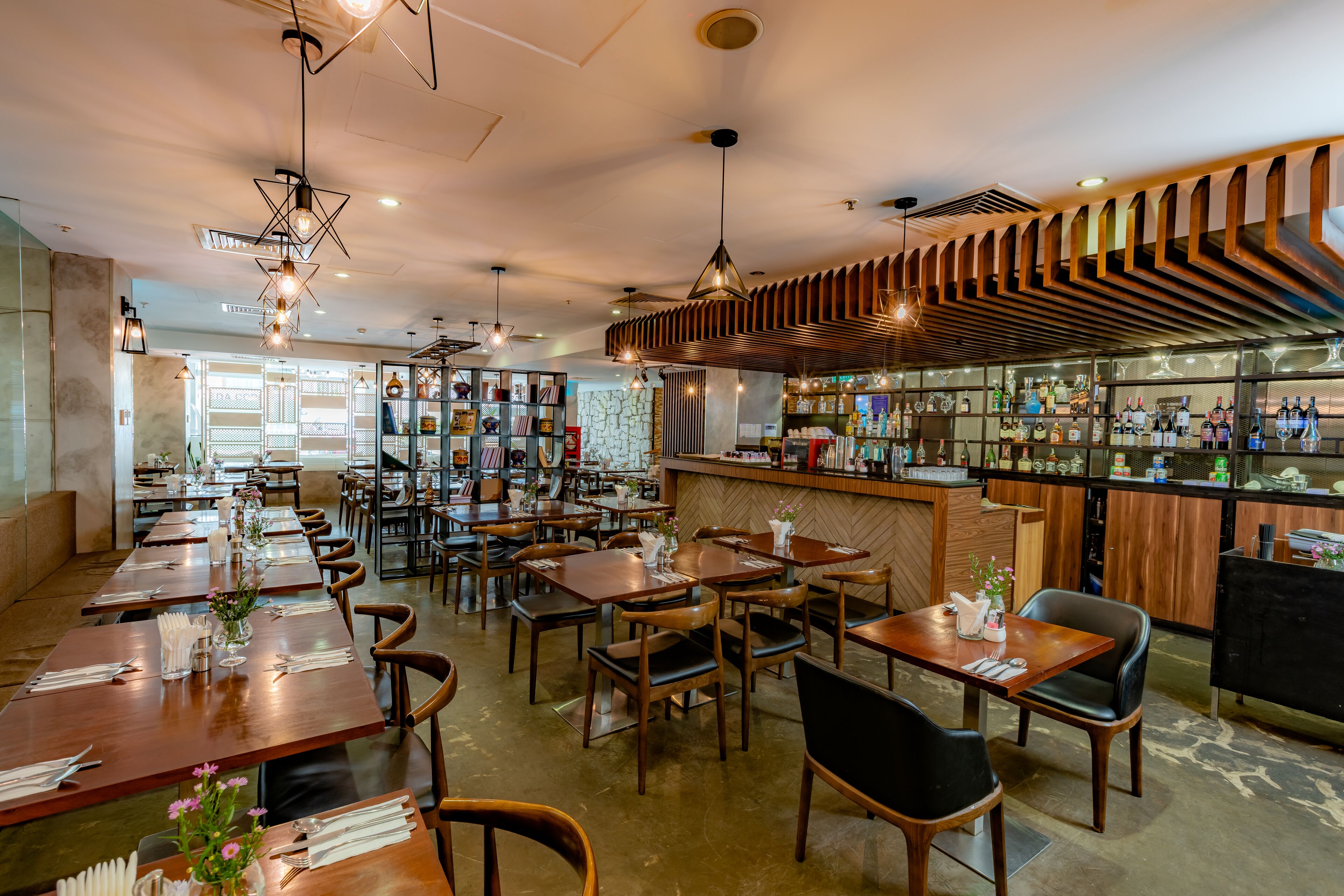 Un restaurante con mesas y sillas de madera, una zona de bar con botellas y vistas a la calle.