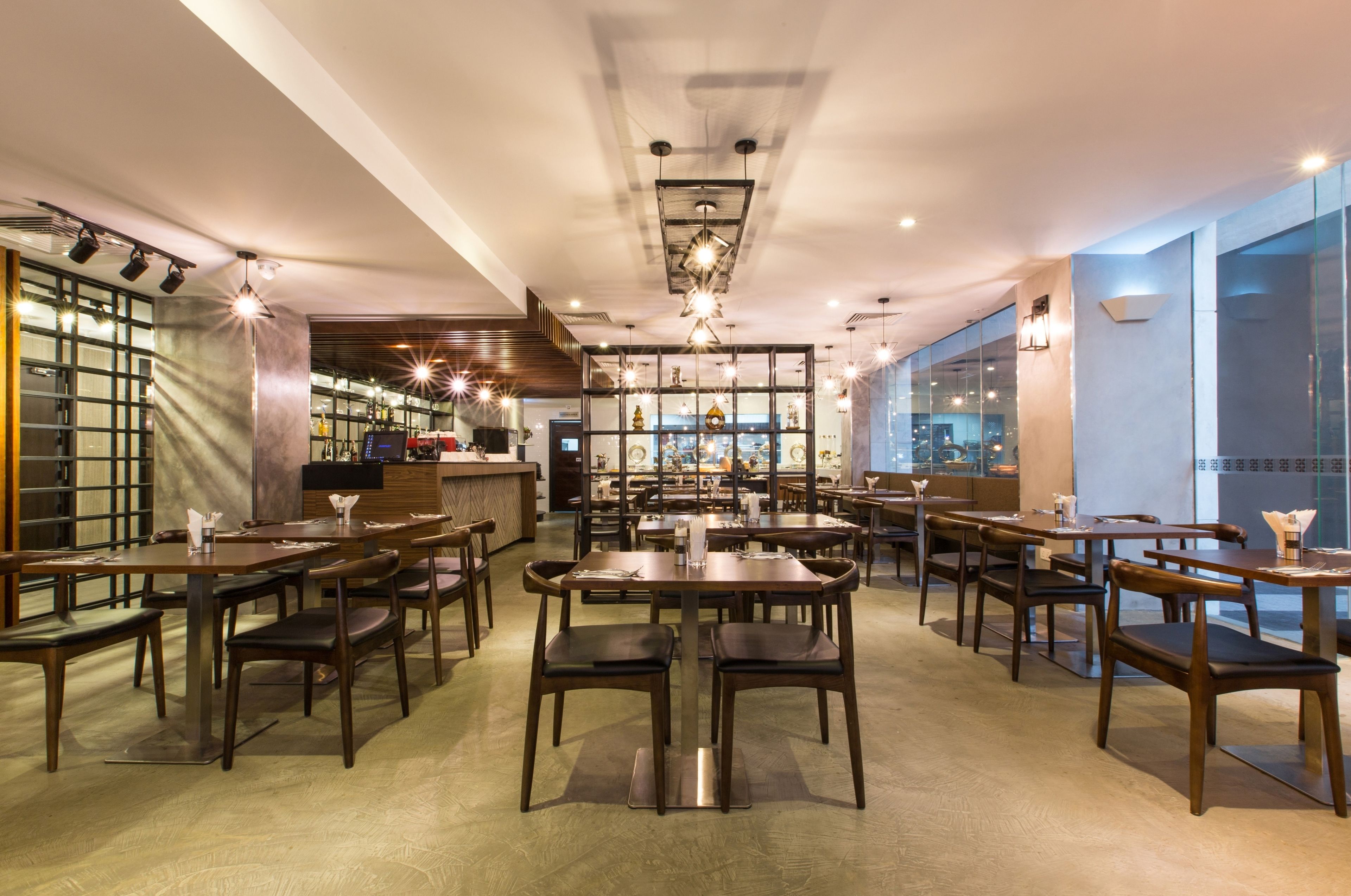 A modern restaurant interior with multiple dining tables and chairs, a bar area, and a view through large windows.