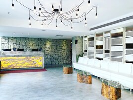 Een moderne lobby met een stenen muur, een receptiebalie en een zithoek met een glazen salontafel.