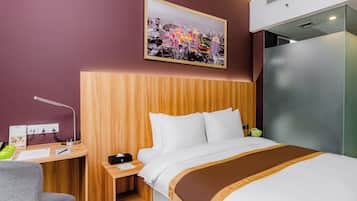 A hotel room with a bed, a desk with a lamp, a nightstand, and a wall-mounted picture.