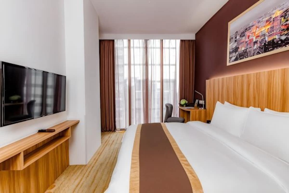 Une chambre d’hôtel dotée d’un grand lit, d’un téléviseur à écran plat, d’un bureau avec une chaise et d’une fenêtre avec des rideaux.