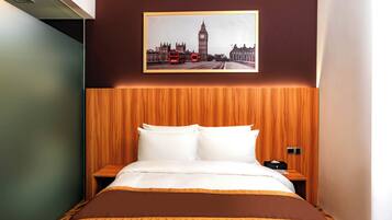 Une chambre d’hôtel avec un lit, une tête de lit en bois, une table de chevet et un tableau représentant Londres accroché au mur.
