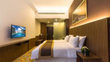 A hotel room with a large bed, a television on the wall, a wooden headboard, and a small table with a vase of flowers.