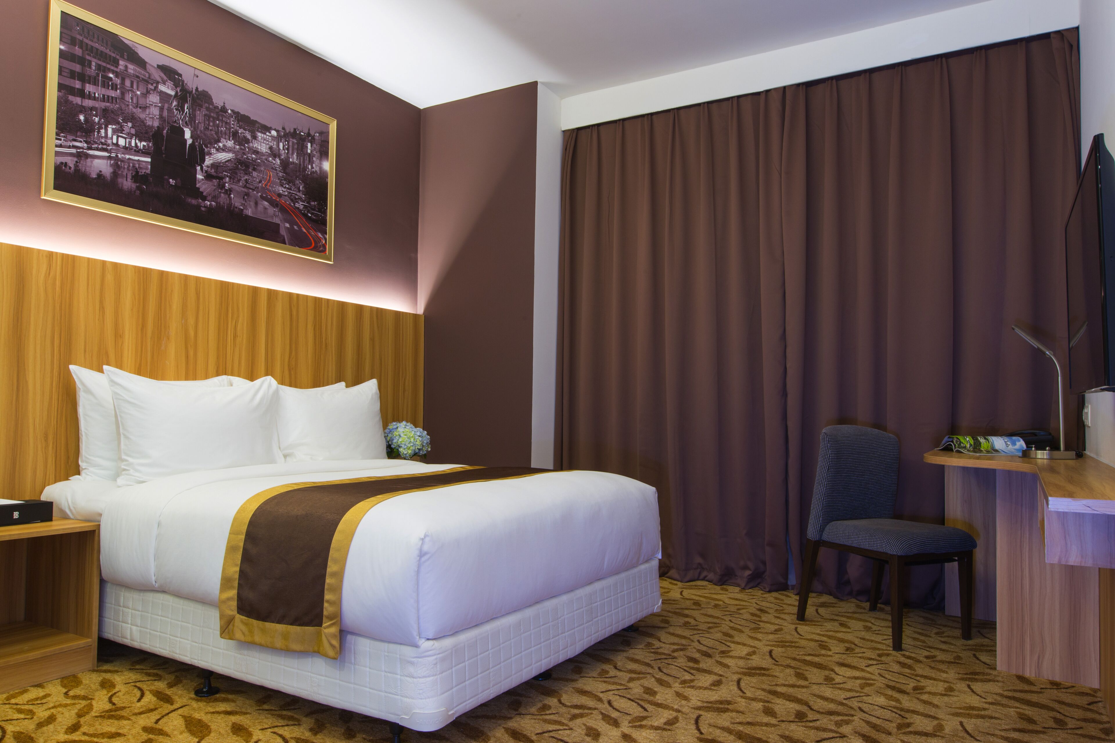 Habitación de hotel con una cama grande, un escritorio con una silla, un televisor y un cuadro en la pared.