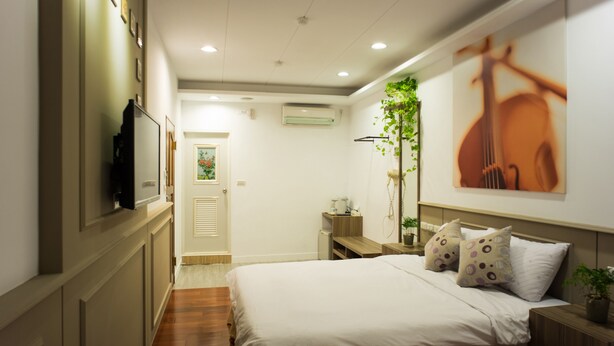 A hotel room with two beds, a TV, a plant, and a painting on the wall. - Bei Pin B&B (Hengchun)