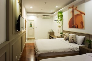 A hotel room with two beds, a TV, a plant, and a painting on the wall.