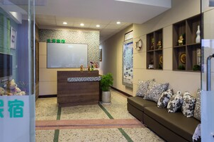 A reception area with a wooden desk, a potted plant, and a sofa with patterned cushions.
