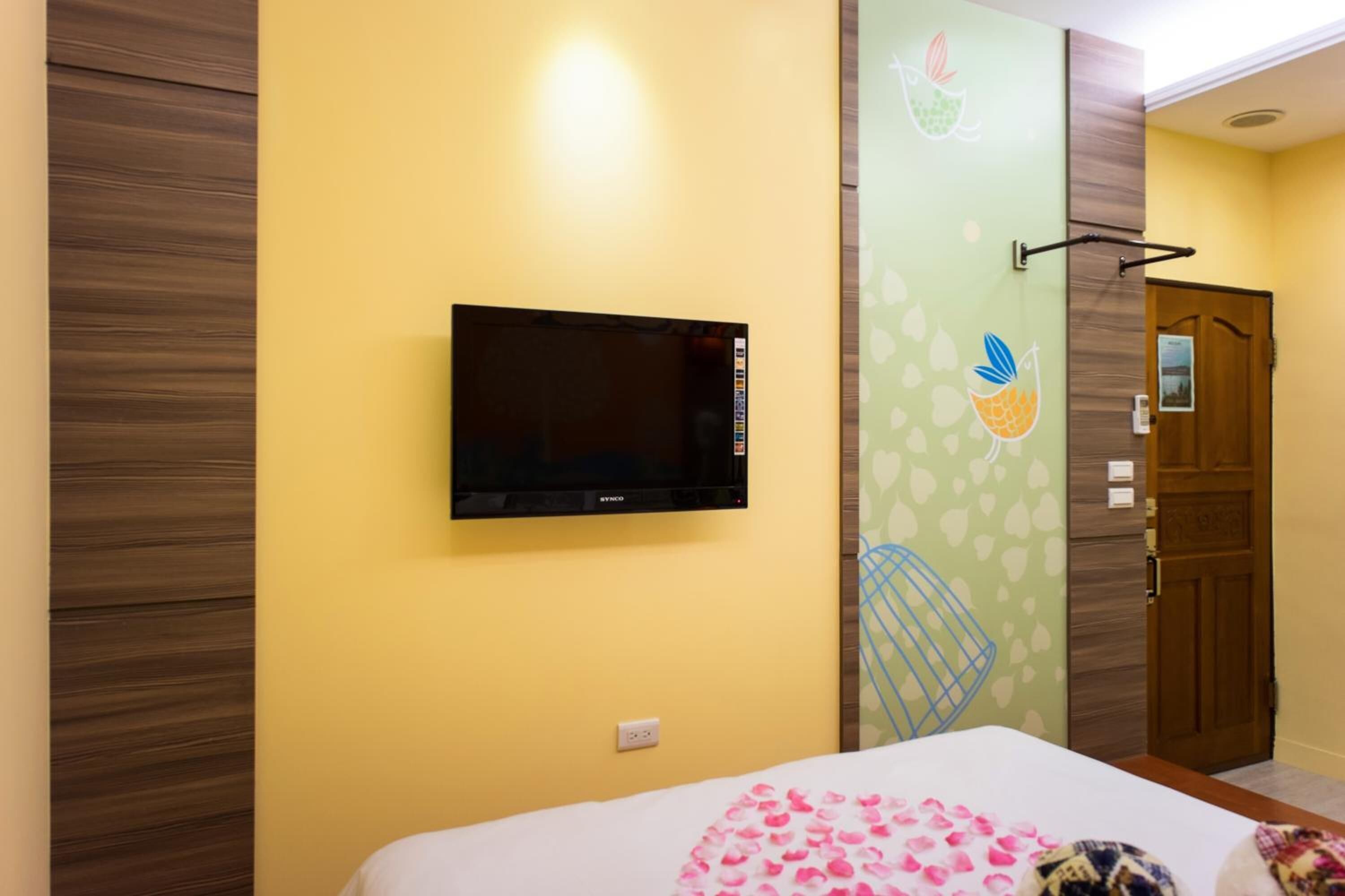 A hotel room with a bed, a mounted television, and a door with a wooden panel.