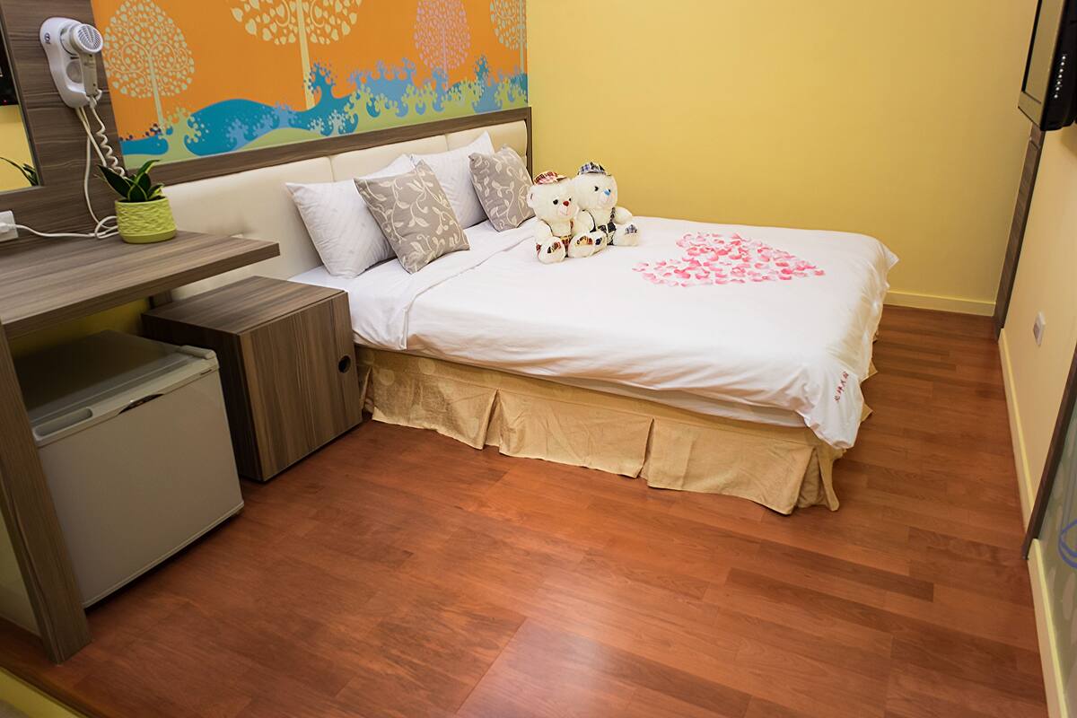Quarto com cama, mesa de cabeceira e um pequeno frigorífico.