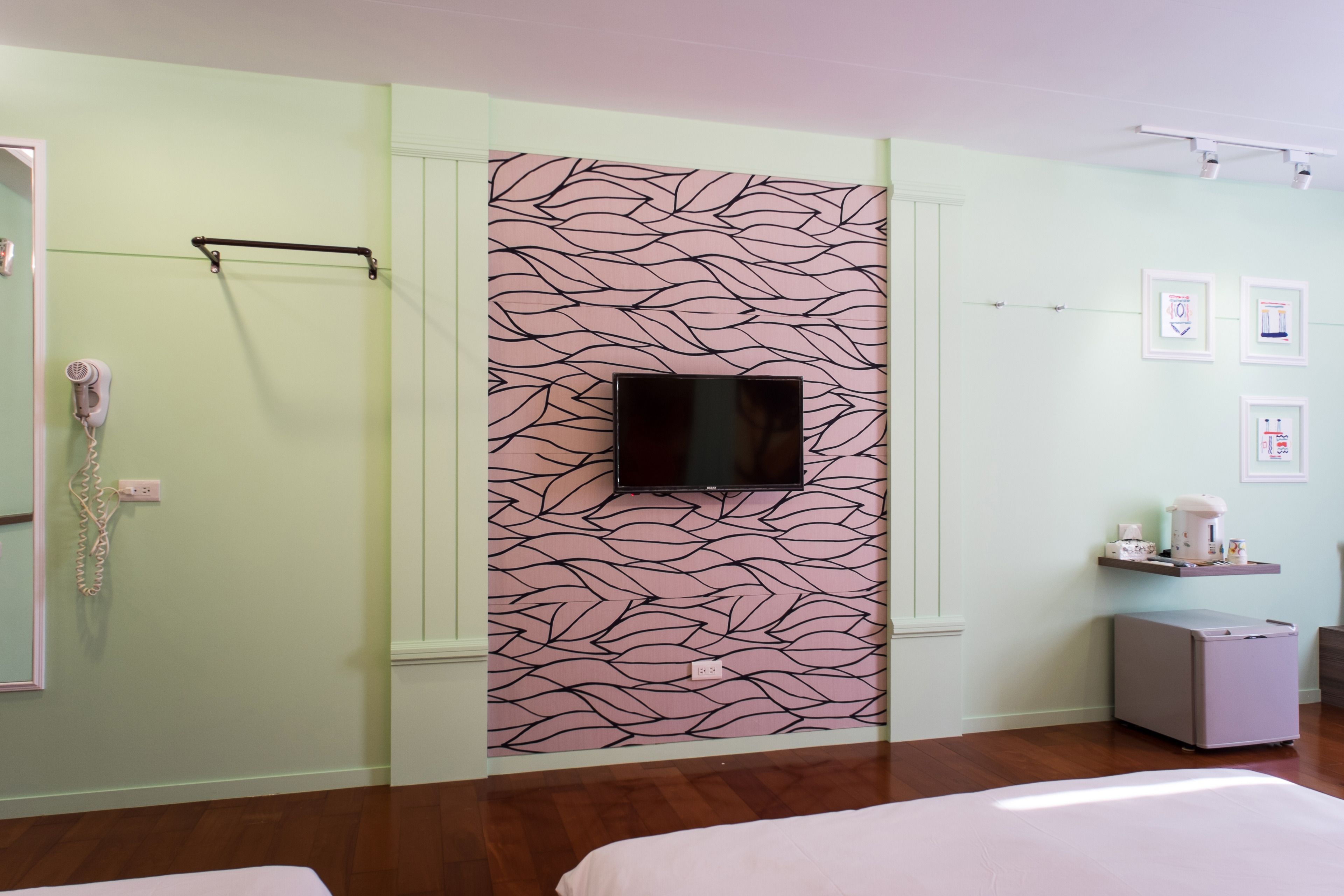 Ein Hotelzimmer mit wandhoher Blättermuster-Tapete, einem Flachbildfernseher, einem kleinen Nachttisch und einem Bett.