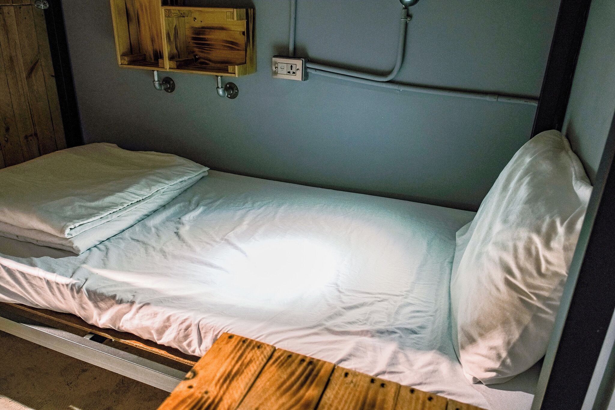 A single bed with white linens, a wooden headboard, and a small wooden table.