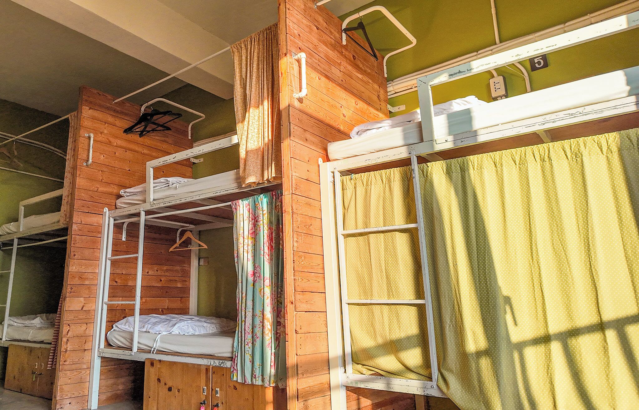 Een slaapkamer met stapelbedden, een houten inrichting, een klein raam met gordijn en een kapstok.