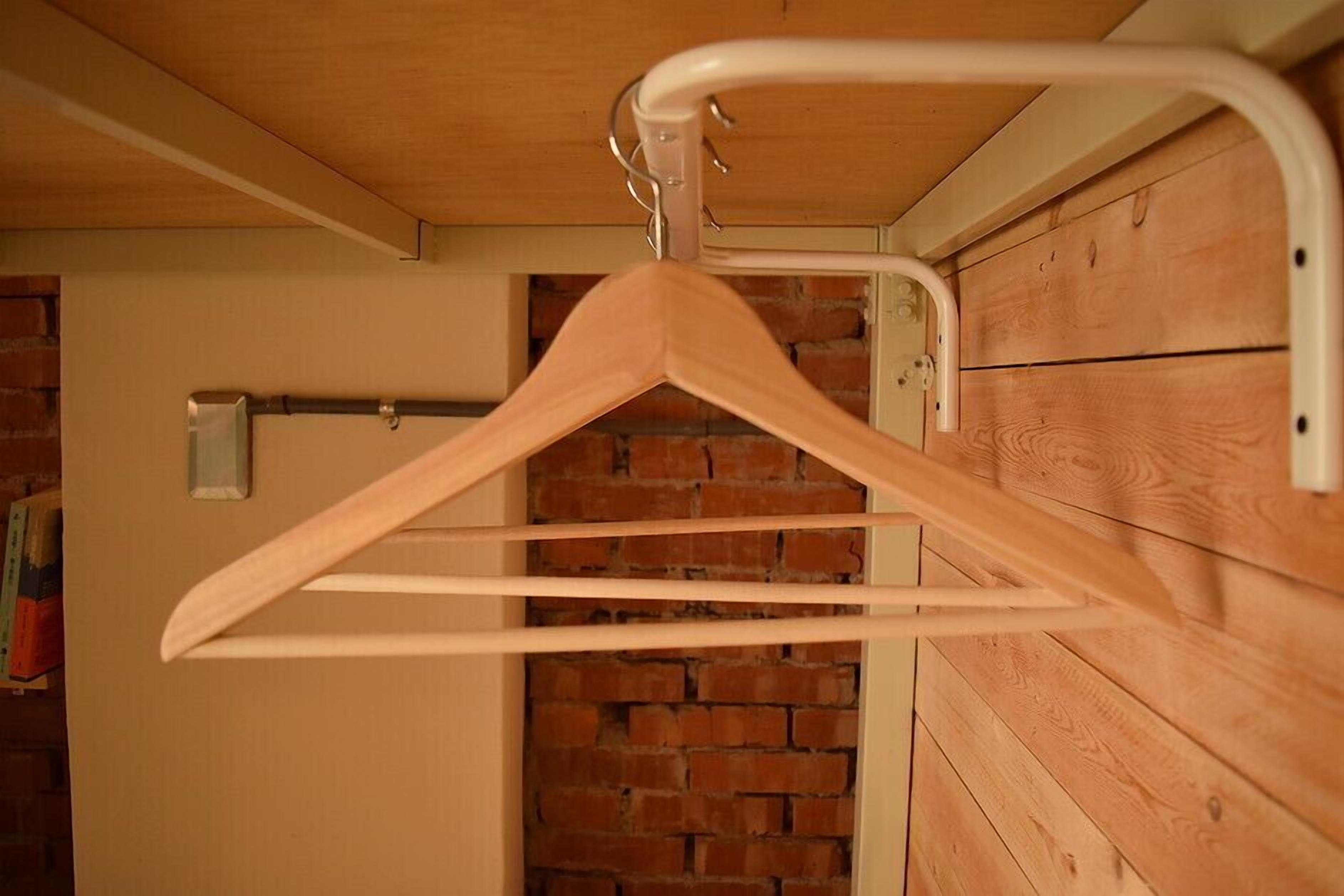 A wooden hanger rack mounted on a wall with a brick wall in the background.